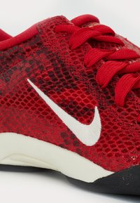 Röd sportskor med en texturerad mesh-övre, vit Nike-swoosh, röda snören och en böjd vit och svart sula.