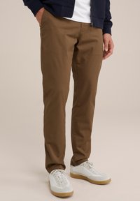 Braune Chinos mit geradem Schnitt, aus weichem Stoff gefertigt. Kombiniert mit weißen Sneakers. Verfügt über Seitentaschen und eine glatte Textur.