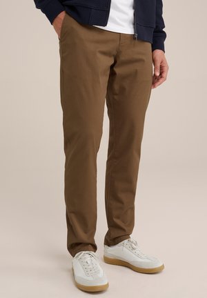 Brown chinos with a straight fit, made of soft fabric. Paired with white sneakers. Features side pockets and a smooth texture.