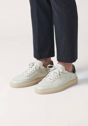 Baskets avec une tige en cuir blanc, une semelle en caoutchouc brun clair et un accent au talon marine. Elles possèdent des lacets ronds et des détails perforés sur l'avant.