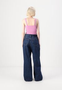 Top de tirantes ancho ajustado de color rosa, combinado con unos vaqueros de mezclilla oscuros y sueltos. Los vaqueros tienen una cintura alta y dos bolsillos traseros.