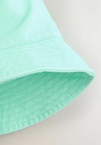 Minzgrüner Hut mit breiter, weicher Krempe. Hergestellt aus strukturiertem Stoff mit horizontalen Streifen. Naht entlang des Krempenrands sichtbar.