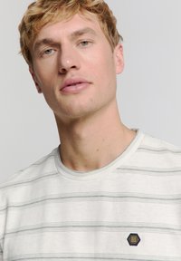 Lichtgrijze gestreepte T-shirt met een ronde halslijn, voorzien van textuurlijnen in de horizontale richting en een klein hexagonaal logo op de borst.