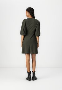 Grønt teksturert kjole med puffermer, innsnevret midje og utsvingt skjørt. Kombinert med svarte ankelstøvletter med blokkhæl.