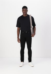Jean noir ajusté, t-shirt noir, baskets blanches, sac messager gris. Tissu lisse, design minimaliste, accents matériels simples.