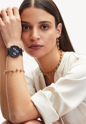 Zwarte horloge met zilveren accenten, gouden ketting en armband, zachte witte blouse met een gladde textuur, close-up van accessoires.