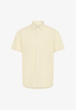 Chemise à manches courtes de couleur beige clair en coton, avec un col pointu, une poche avant et une fermeture à boutons, texture de tissu lisse.