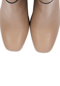Stivaletti alla caviglia beige in pelle con punta affilata, texture liscia e dettaglio in pizzo nero lungo il bordo superiore. Design semplice e lineare.