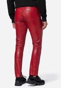 Rode leren broek met een aansluitend ontwerp, zichtbare stiksels en vijf zakken. Compleet met een zwart sweatshirt en dikke zwarte sneakers.