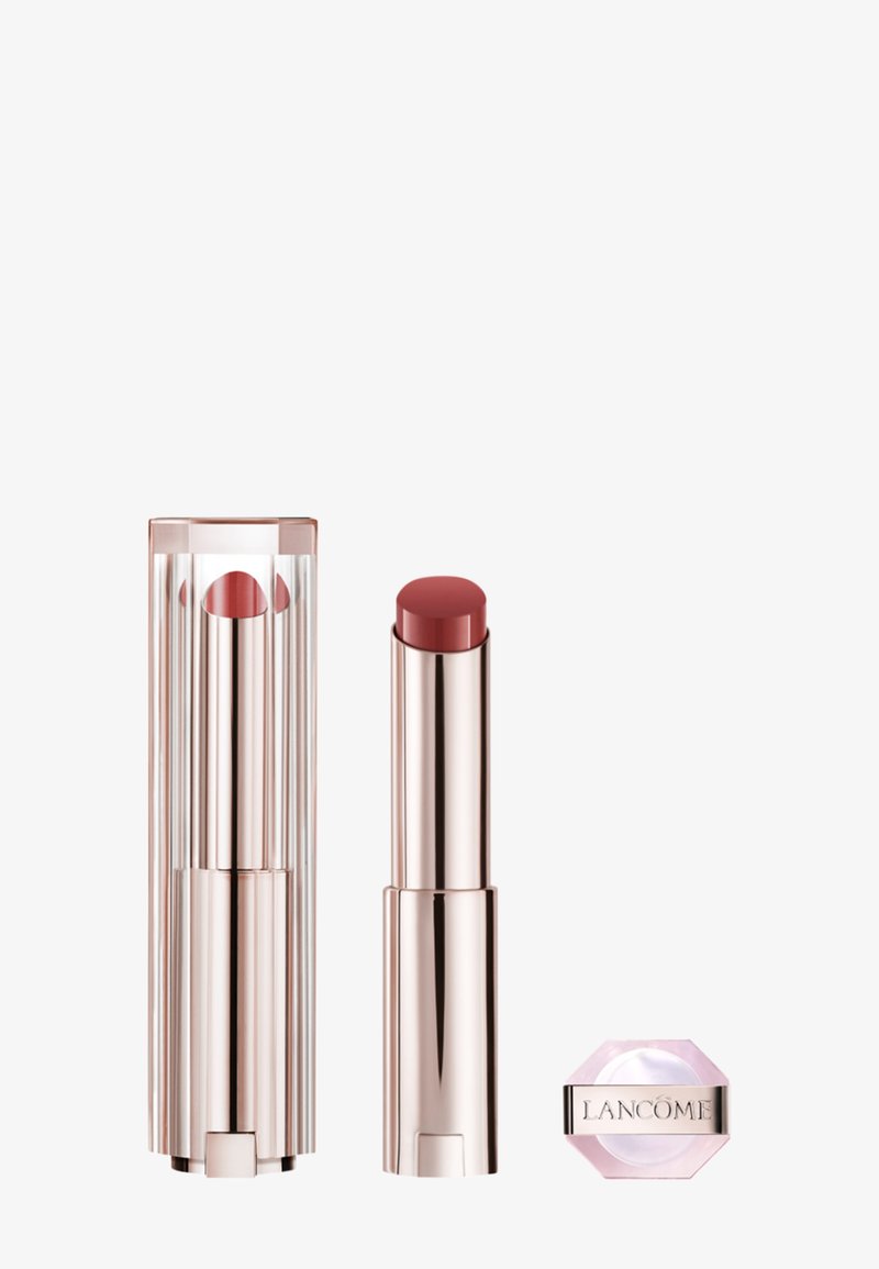 Rouge à lèvres rose dans un tube en métal élégant et brillant à côté d'un compact hexagonal rose avec un logo argenté. L'étui transparent présente des rayures verticales.