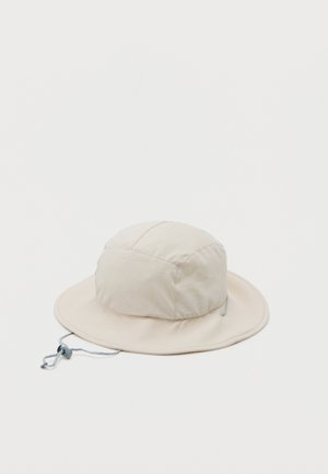 Chapeau bob beige clair avec large bord et cordon de réglage sous le menton sur fond blanc uni.