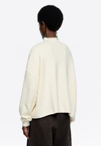 Cremfarbener Fleece-Pullover mit lockerer Passform, abgesenkten Schultern und hohem Kragen, der eine weiche Textur und gerippte Bündchen aufweist.