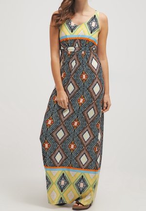 Kvinde iført ærmeløs maxikjole med flerfarvede geometriske diamantmønstre i orange, blå, gul, sort og hvid.
