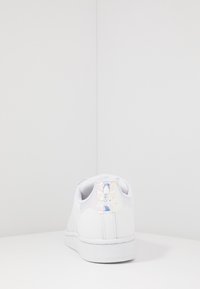 White sneaker with a smooth synthetic upper, textured side panels, and reflective logo on heel. Features a rubber sole and cushioned collar.