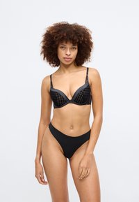 Conjunto de lingerie preto com um sutiã texturizado de padrão xadrez e uma roupa interior simples, ambos feitos de um tecido liso e elástico.