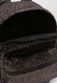 Sac à dos noir texturé et métallique avec une surface brillante, doté d'un compartiment principal zippé et d'une doublure en tissu doux et foncé.