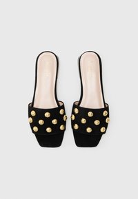 Black suede slide sandals featuring a wide strap adorned with gold studs. The insole is light beige with a subtle logo. Squares toe design.