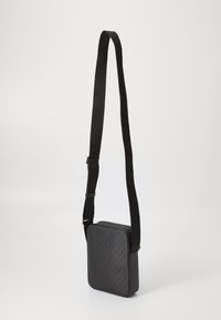 Borsa a tracolla nera di forma quadrata, realizzata in pelle liscia, con chiusura a zip e un motivo testurizzato sulla parte anteriore. Inclusa tracolla regolabile.