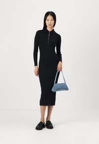 Abito midi nero a coste con maniche lunghe e colletto, caratterizzato da dettagli con bottoni. Abbinato a una borsa azzurro chiaro e scarpe nere.