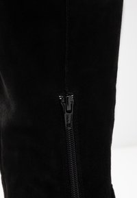 Czarne zamszowe kozaki za kolano z błyszczącym, czarnym zamkiem błyskawicznym po boku, o gładkiej teksturze i dopasowanym fasonie.