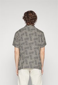 Krátký rukáv košile v černobílém geometrickém vzoru, s rozepnutým límcem a volným střihem, vyrobená z lehké látky.