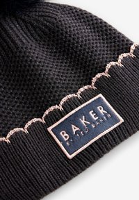 Musta neulottu pipo, jossa on vaaleanpunainen aaltoileva reunus ja suorakaiteen muotoinen Baker by Ted Baker -kangasmerkki ommeltuna resorin kohdalle.