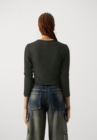 Haut à manches longues côtelé vert foncé avec un col rond, associé à un pantalon cargo en jean bleu taille haute doté de grandes poches arrière.