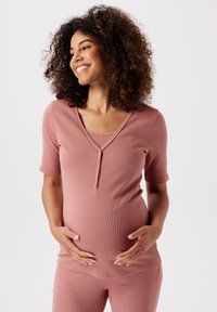 Zwangere loungewear set in zachtroze geribbeld materiaal, met een top met korte mouwen en een ronde halslijn en bijpassende strakke broek.