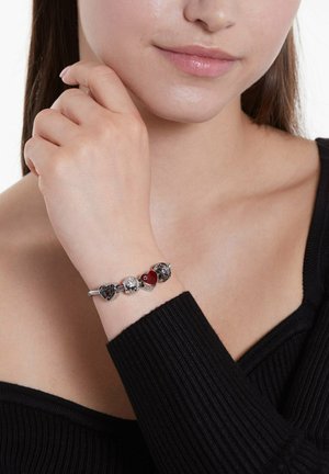 Silver charm bracelet featuring heart-shaped and round charms in red, black, and clear designs, set against a textured black top.