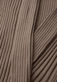 Gros plan sur un tissu en maille côtelée taupe avec des lignes texturées verticales et des sections pliées.
