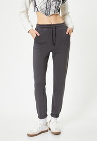Grijze sweatpants van zacht materiaal, met een elastische tailleband, zijzakken en taps toelopende boorden. Gestyled met witte sneakers.