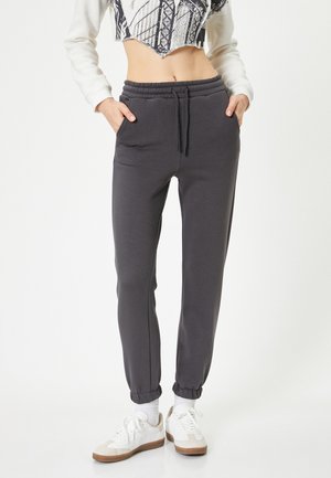 Grijze sweatpants van zacht materiaal, met een elastische tailleband, zijzakken en taps toelopende boorden. Gestyled met witte sneakers.