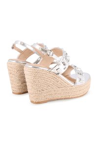 Sandalias de cuña plateadas con suelas de yute trenzado, decoradas con tachuelas ornamentales en las correas y hebilla ajustable en el tobillo. Acabado metálico suave.
