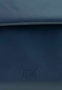 Borsa rettangolare blu navy realizzata in tessuto liscio. Presenta una chiusura a pattina e un logo "JOST" impresso sulla parte anteriore. Superficie testurizzata.