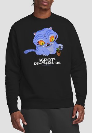 Black sweatshirt featuring a cartoon blue cat with large yellow eyes and fangs, holding a small potted plant. Text reads "KPOP DEMON HUNTERS."