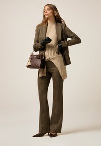 Un costume marron à carreaux avec un pantalon évasé et un long blazer, associé à un haut beige. Des gants en cuir noir et un sac à main brun foncé sont inclus.