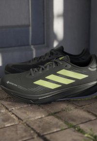 Par sive sivih i neonsko žutih tenisica za trčanje s Gore-Tex i DreamStrike oznakama na popločanom otvorenom području.