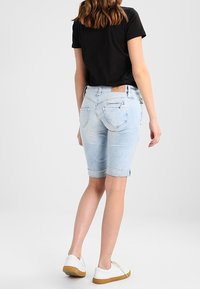 Shorts en denim bleu clair avec ourlets retroussés, dotés de poches arrière avec des détails subtils, associés à un t-shirt noir ajusté et des baskets blanches.