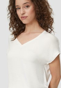 Maglietta bianca a collo a V con maniche corte, tessuto morbido, vestibilità comoda, caratterizzata da un piccolo logo accanto all'orlo, design minimalista.