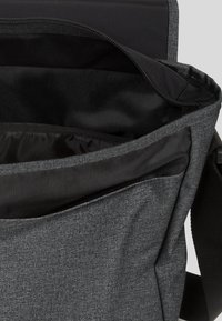 Šedá textilní messenger taška se zipovým otevíráním, černou podšívkou a hladkým povrchem. Obsahuje boční kapsu pro další úložný prostor.