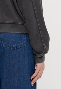 Sudadera gris oscuro con un corte relajado, puños acanalados y una textura suave, combinada con unos pantalones de mezclilla azul de corte clásico.
