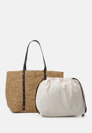 Hellbraune gewebte Tragetasche mit schwarzen Griffen neben einem beigefarbenen Beutel mit Kordelzug und schwarzen Bändern auf weißem Hintergrund.