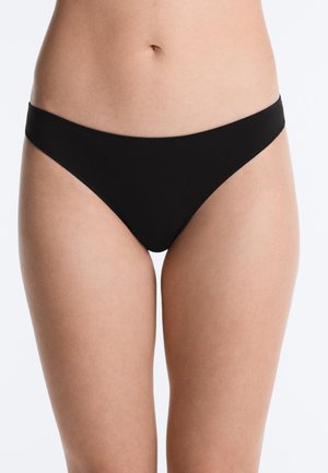 Femeie care poartă lenjerie neagră fără cusături în stil bikini, prezentată de la talie până la mijlocul coapsei pe un fundal alb.