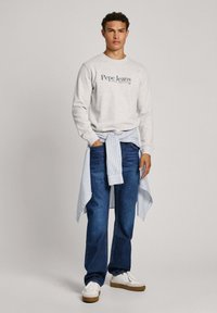 Sivi dukserica s logotipom "Pepe Jeans", plavi traperice i plava i bijela prugasta košulja vezana oko struka; bijele cipele s bež potplatima.