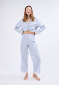 Conjunto de pijama a rayas azul claro con mangas largas, top cortado y pantalones de corte holgado que presentan detalles de encaje en los puños. Textura de tela suave.