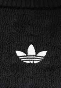 Čierna pletená čiapka s bielym logom Adidas, ktoré obsahuje tri vodorovné pruhy a prvky listového dizajnu. Textúrovaný povrch látky.