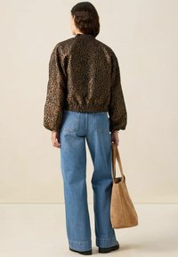 Veste bomber en imprimé léopard marron avec des poignets élastiques, associée à un jean bleu taille haute et un sac à épaule en daim beige. Texture lisse.