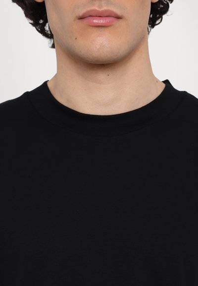 Camiseta de algodón negra con cuello redondo, textura suave y sin patrones ni herrajes visibles. Diseño simple y minimalista.