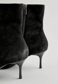 Schwarze Wildleder-Ankle Boots mit einem eleganten Design, ausgestattet mit einem Reißverschluss und einem schlanken Stiletto-Absatz. Geschmeidige Textur und minimalistischer Stil.