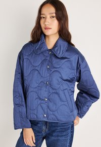 Κουβερτίνα μπλε μπουφάν με φαρδιά γιακά, κουμπιά κλείστρου και υφή κυματιστού σχεδίου; διαθέτει μακριά μανίκι α και κοντή εφαρμογή.